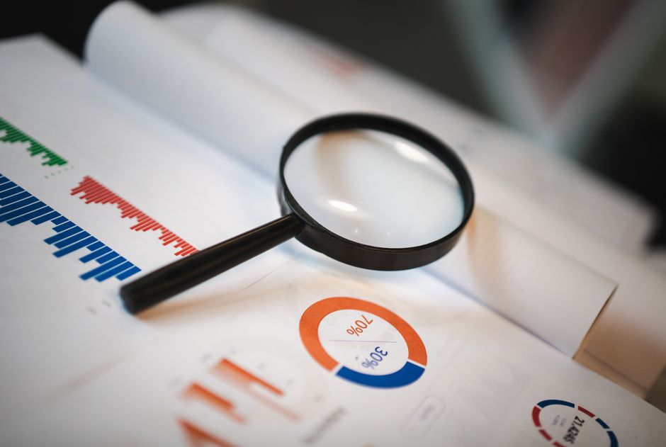 A magnifying glass over a printed report with charts and graphs