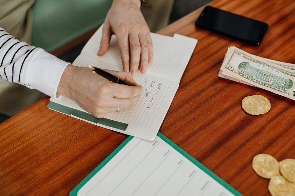 A person writing a budget checklist next to cash and coins